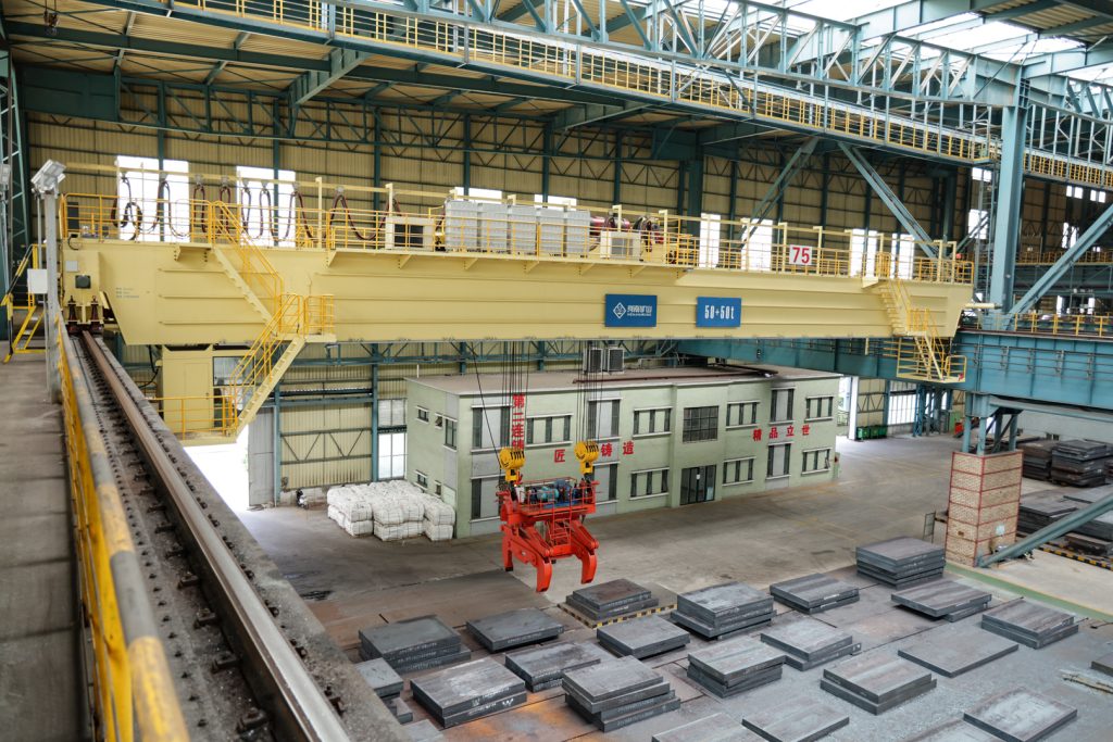 Henan Mine Crane heavy-duty overhead crane with a mechanical slab clamping attachment in a steel plant